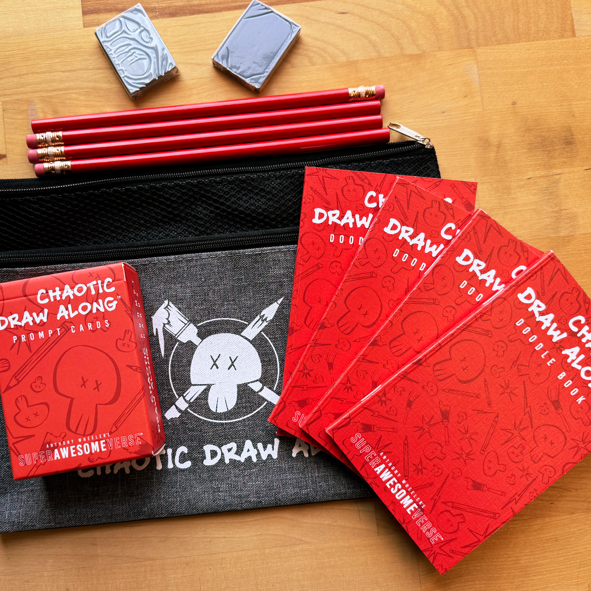Chaotic Draw Along family night bundle featuring prompt cards, red doodle books, pencils, erasers, and a branded pencil case arranged on a wooden table.