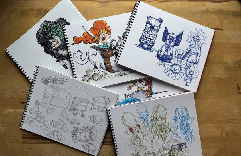 Open sketchbooks spread across a wooden table with colorful Chaotic Draw Along character drawings, sketches, and creative art studies.