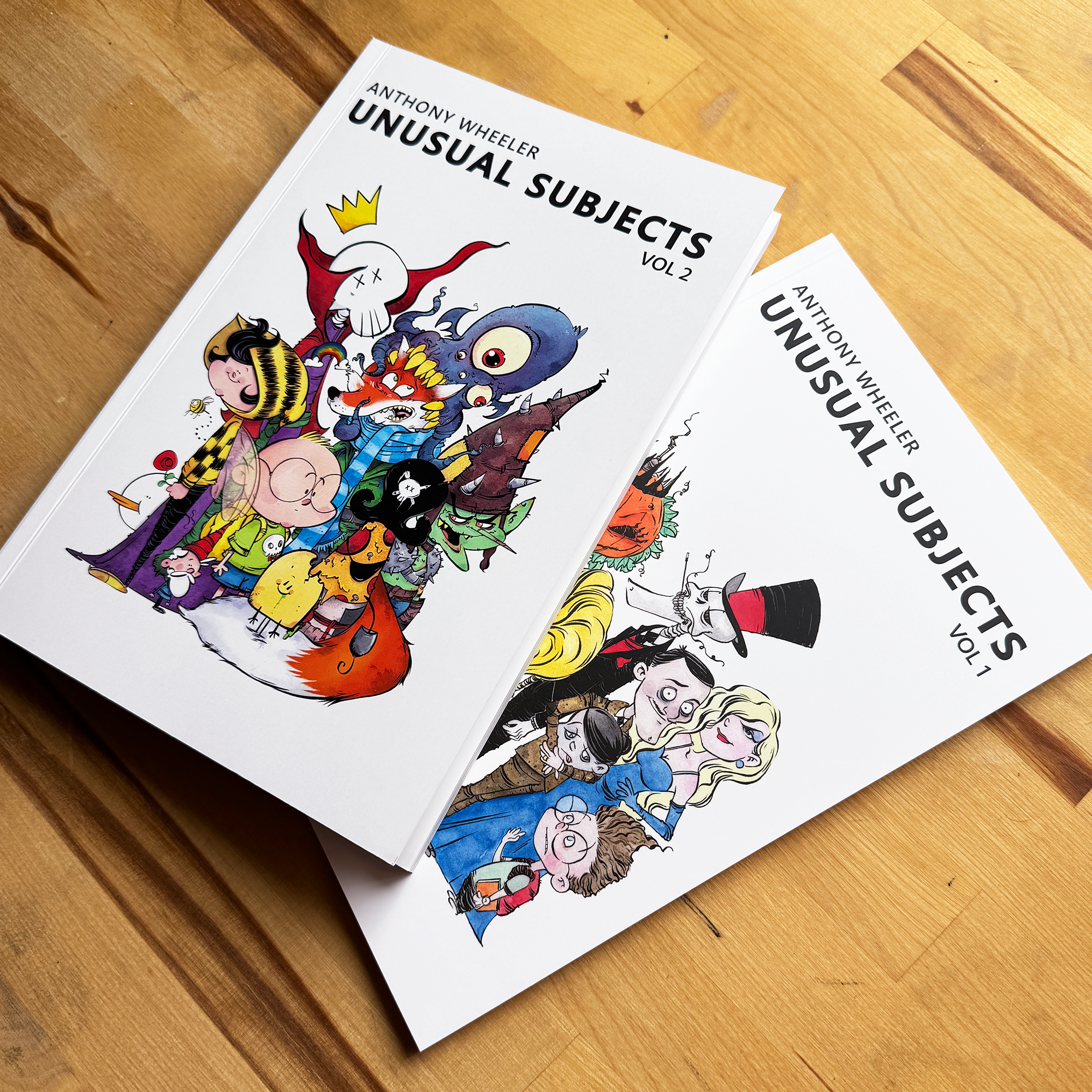 Anthony Wheeler’s Unusual Subjects Vol. 1 and Vol. 2 art books displayed together on a wooden tabletop.
