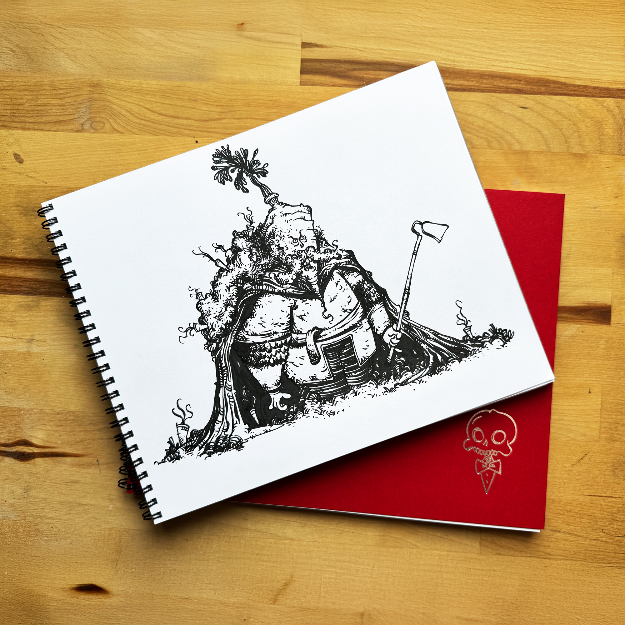 Spiral-bound sketchbook with a detailed black ink character illustration on top of a red notebook, displayed on a wooden table.